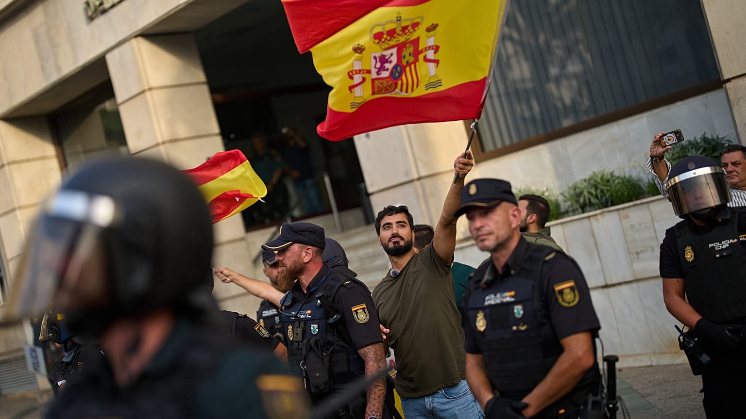 Far-right politician Alvise Pérez waves a Spanish flag under police protection while Ceuta residents protest his presence on Saturday 1 August