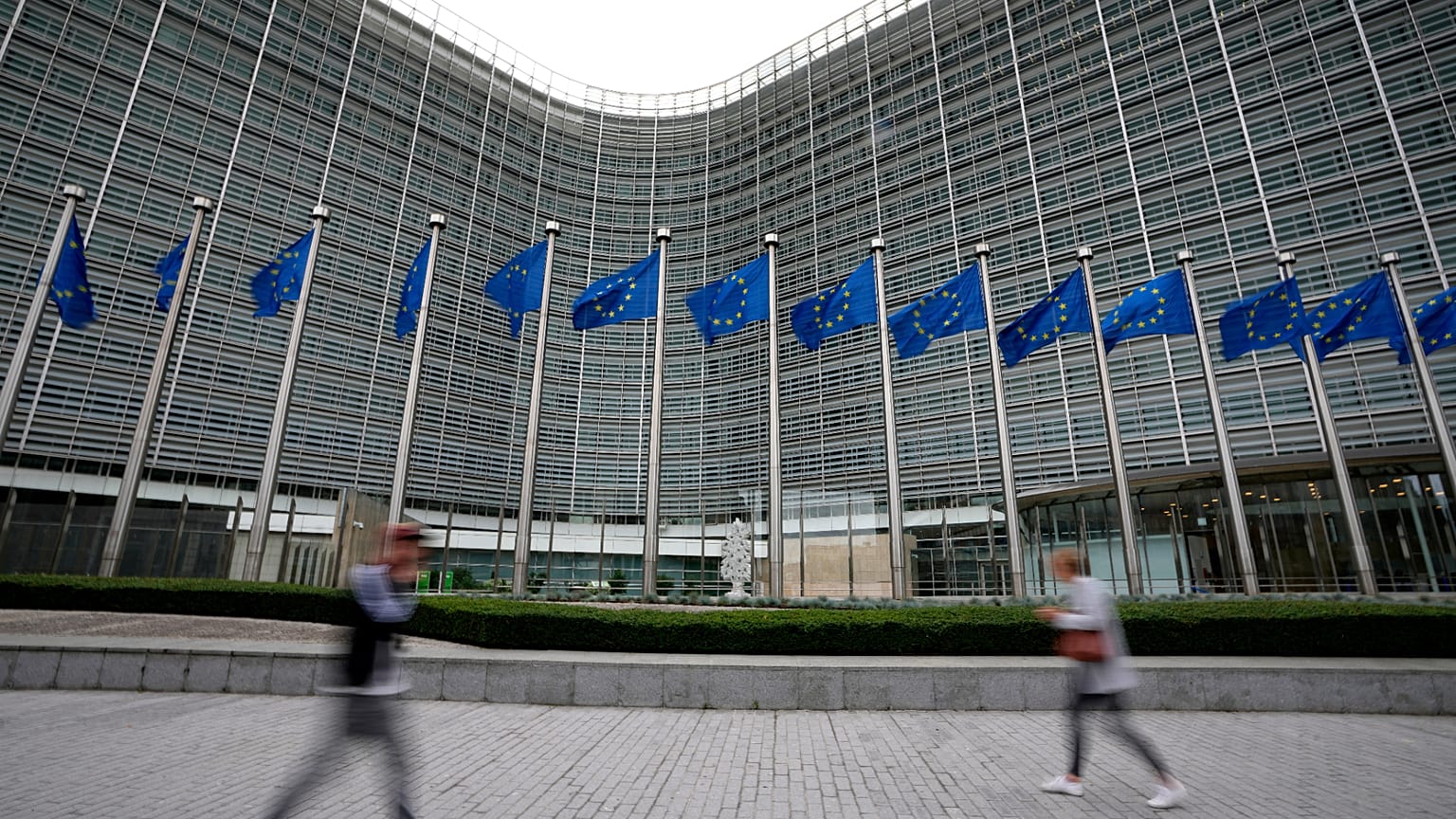 FILE - European Union flags flap in the wind as pedestrians walk by EU headquarters in Brussels. Sept. 20, 2023. 