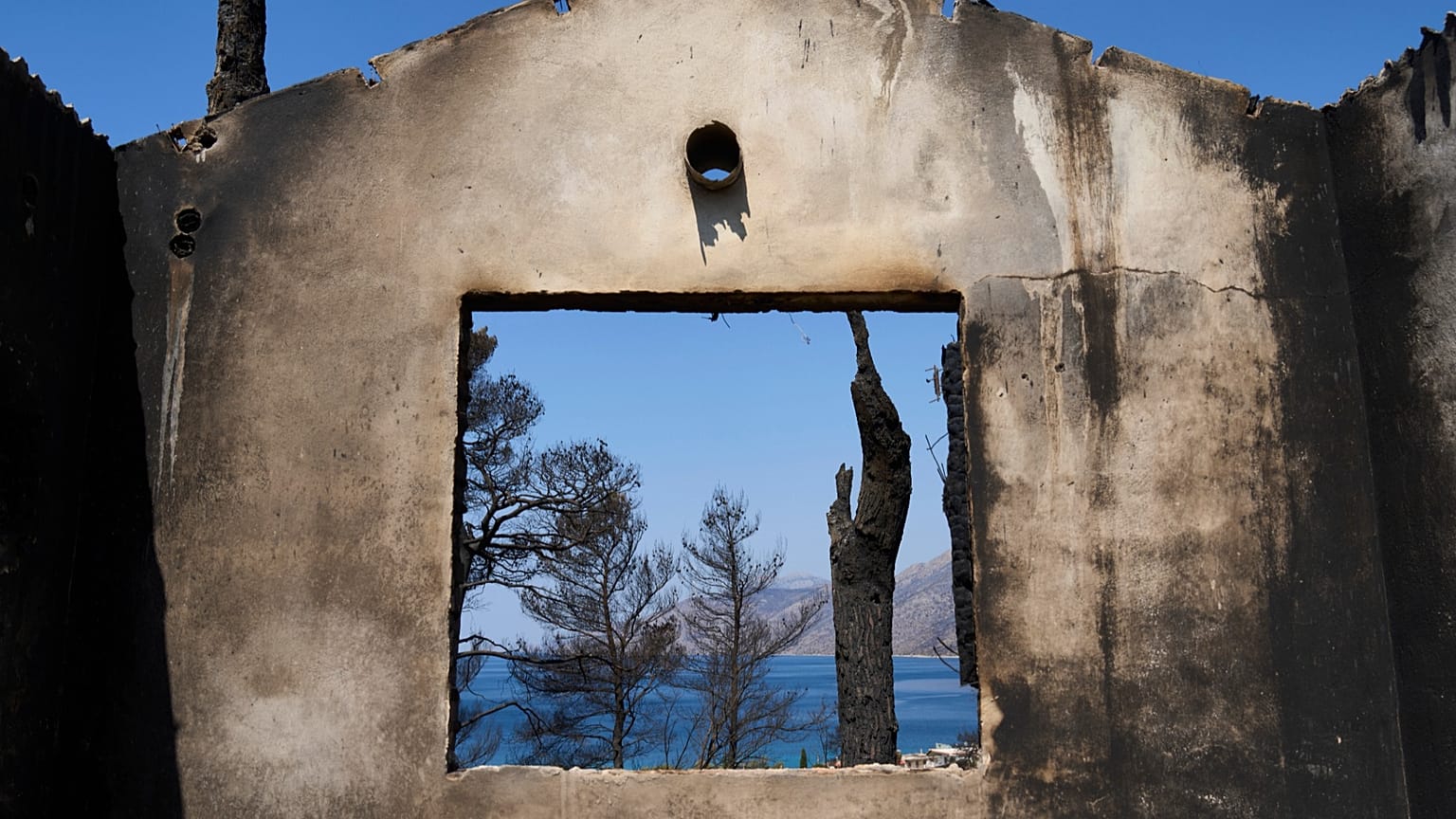 The sea is visible through the remains of a house destroyed by a wildfire in Porto Germeno, 4 August, 2026