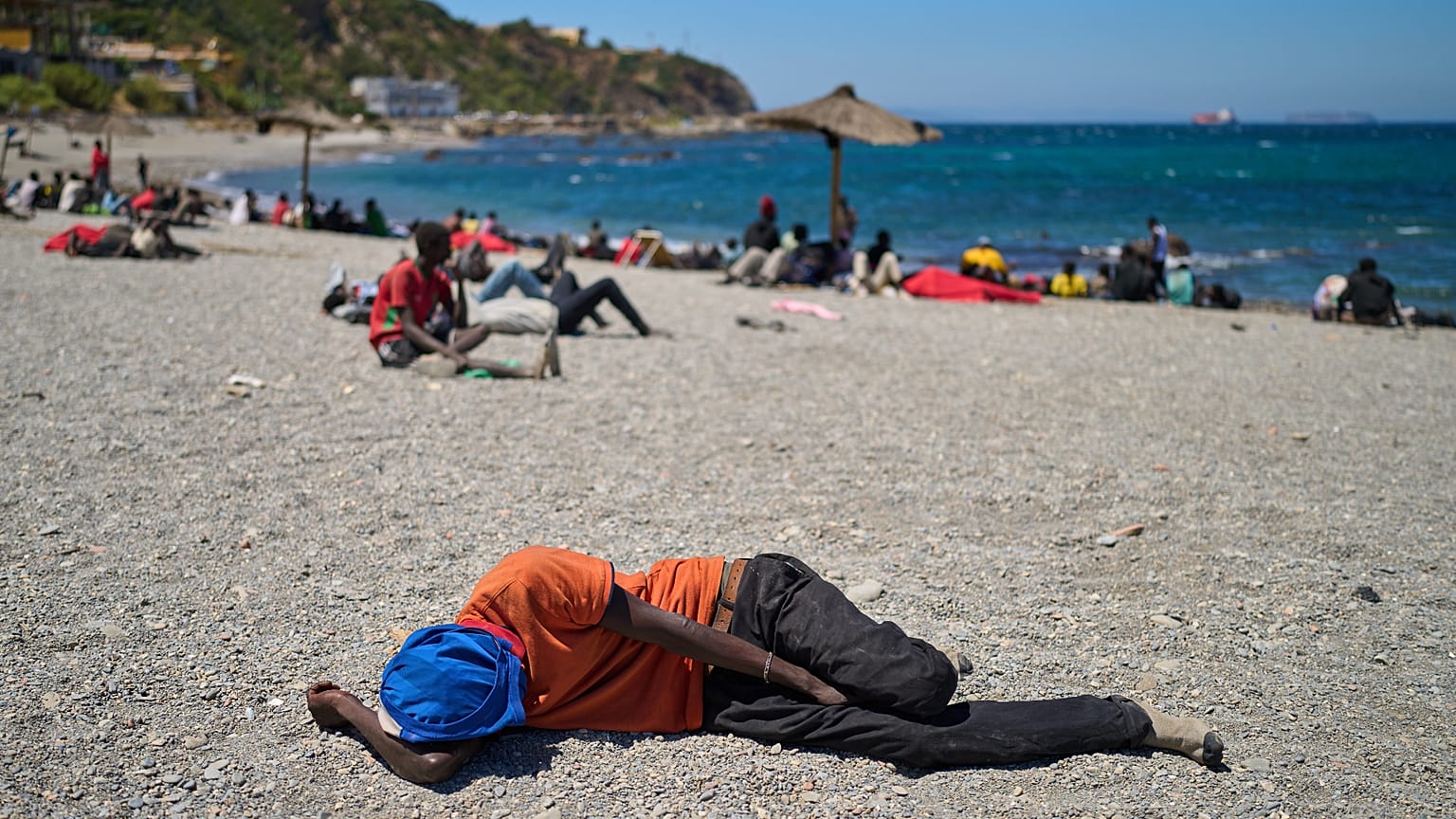 A migrant who crossed into Spain from Morocco sleeps on a beach in the Spanish enclave of Ceuta on Sunday, 2 August 2026. (AP Photo/Bernat Armangue)